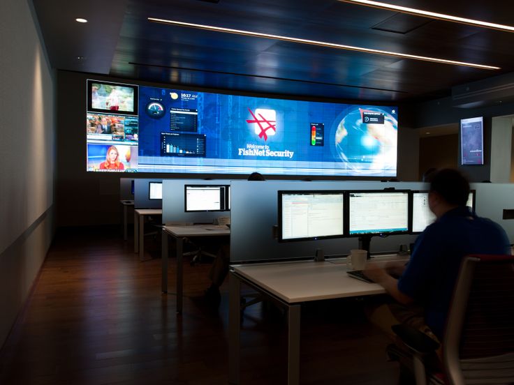 a man sitting at a desk in front of multiple computer monitors with screens on the wall