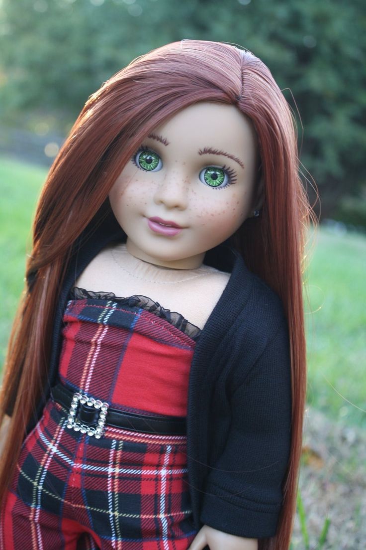 a doll with long red hair and green eyes is standing in the grass wearing a black cardigan