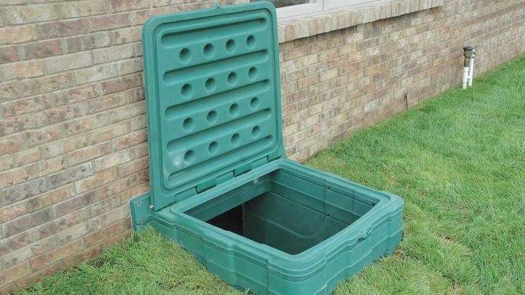 a green cooler sitting in the grass next to a brick wall