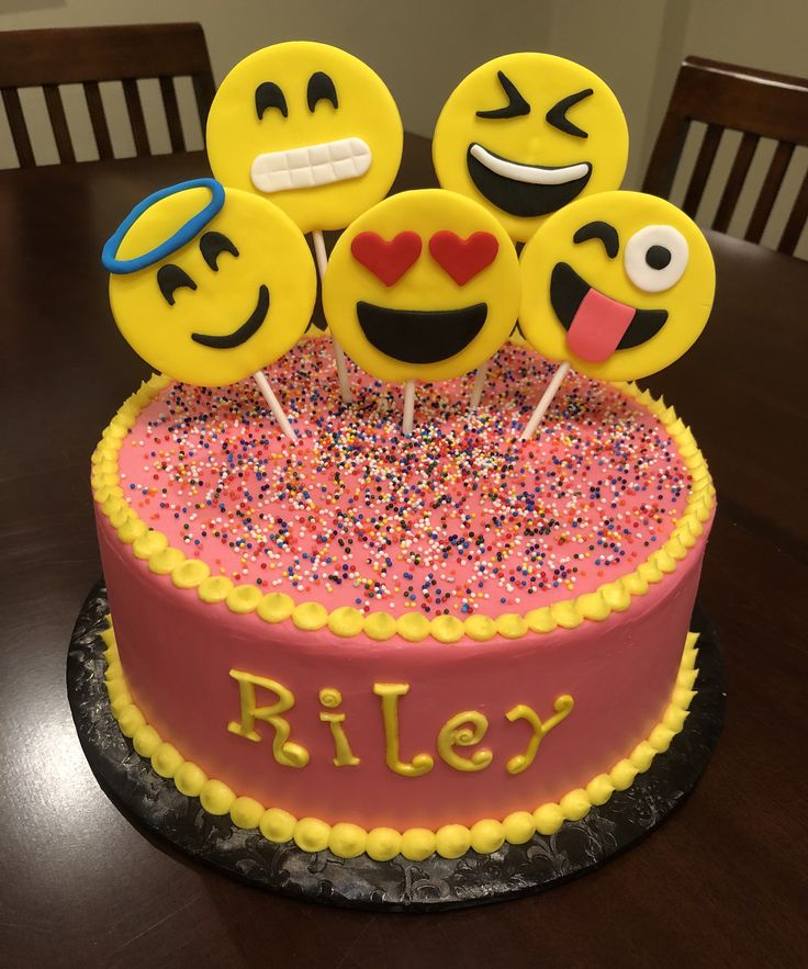 a birthday cake decorated with smiley faces and sprinkles on a wooden table