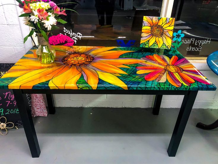 a table with flowers painted on it in front of a store window, next to a flower vase