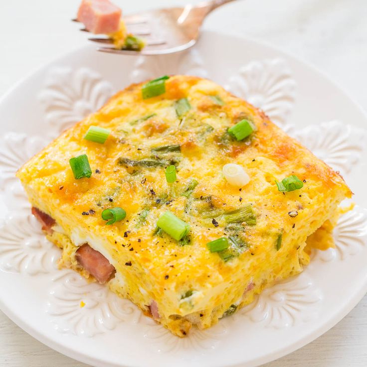 a white plate topped with an omelet covered in cheese and green onions next to a fork