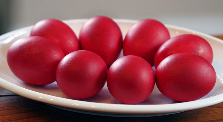 six red eggs in a white bowl on a wooden table