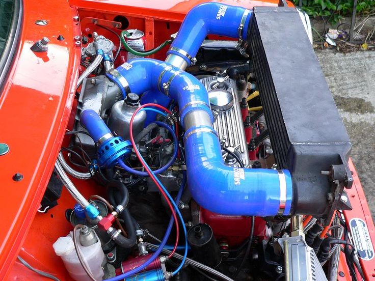 the engine compartment of an orange car with blue hoses