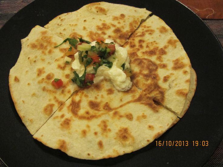 a tortilla on a black plate topped with cheese and veggies