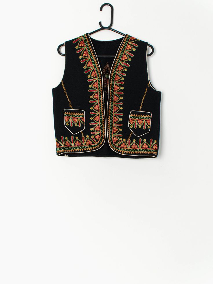 Vintage embroidered waistcoat in black with colourful pattern. This stunning waistcoat features two open pockets and a hook-and-eye closure. Circa 1950 - 1970. Made from a lightweight soft wool that can be worn both this winter and festival season!   Our recommended size: Medium Label says: No size label Condition: Very good Material: No care label, confident it is wool Measurements in inches: Pit to pit: 18.5 Shoulders: 13.5 Hem: 18.5 Front length: 20.5 Back length: 20 We recommend that you com Winter Bohemian Black Vest, Bohemian Black Embroidered Vest, Traditional Black Sleeveless Vest, Folk Style Black Outerwear For Festivals, Black Folk Style Outerwear For Festivals, Black Folk Outerwear For Festivals, Black Folk Style Festival Vest, Traditional Black Vest For Festival, Vintage Black Vest Outerwear