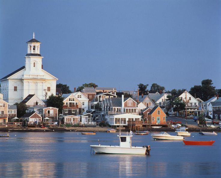 several boats floating on the water in front of some houses and a church with a steeple