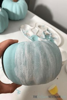 a person holding a painted pumpkin in front of some other blue and white pumpkins