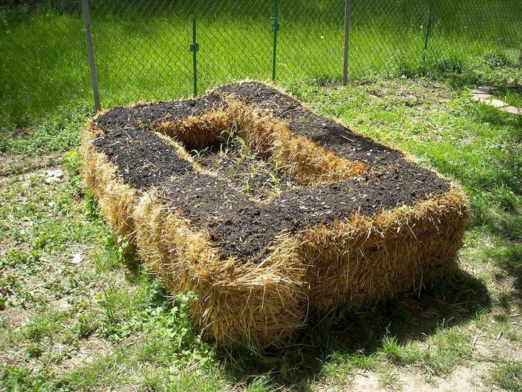 a pile of hay sitting in the middle of a field next to a chain link fence