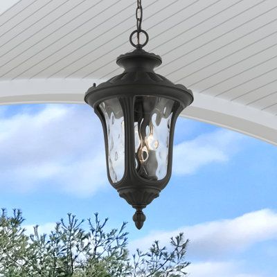 an outdoor light hanging from the side of a porch with trees and blue sky in the background