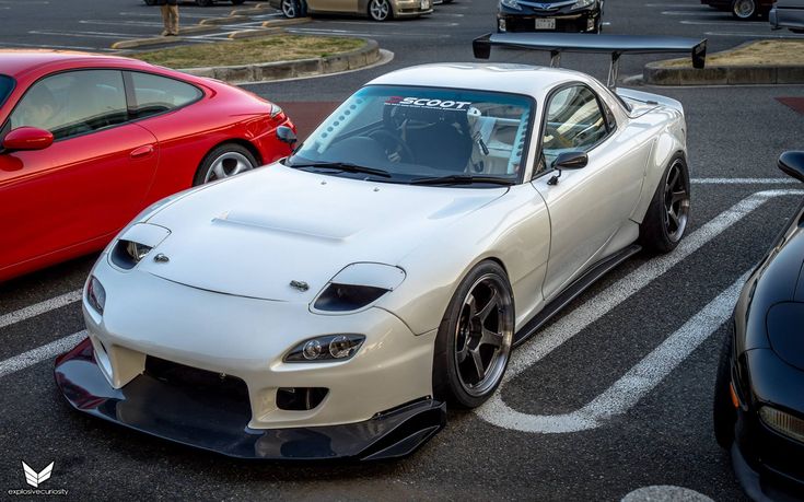 a white sports car parked in a parking lot next to two red and one black cars