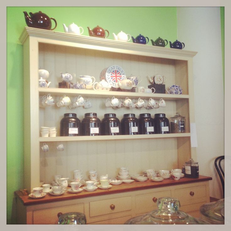 a shelf filled with lots of cups and saucers on top of wooden shelves next to a green wall