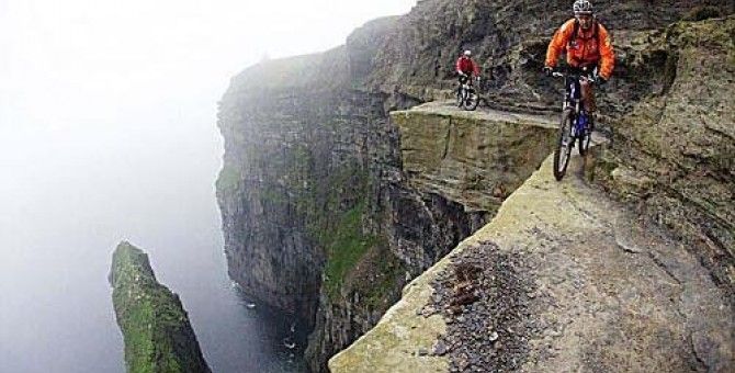 two mountain bikers ride along the edge of a cliff