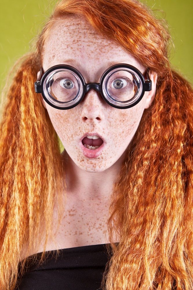 a woman with red hair and glasses making a surprised face while looking at the camera