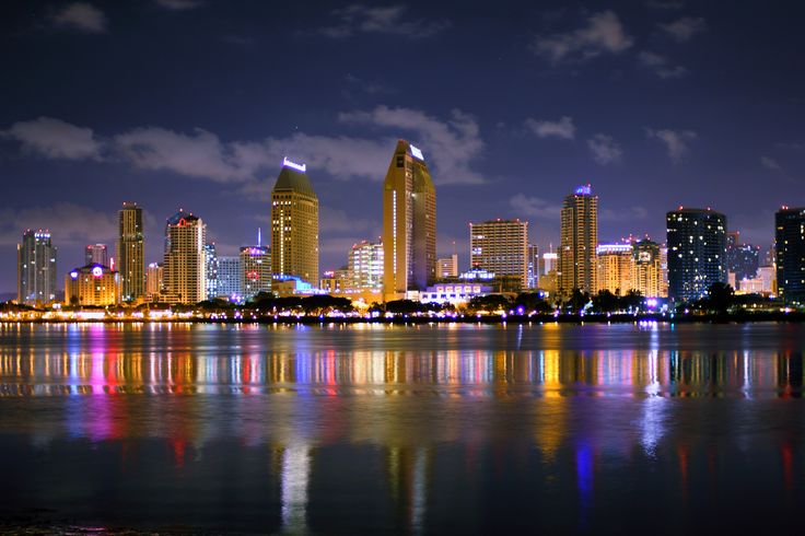 the city is lit up at night with bright lights on it's buildings and reflecting in the water