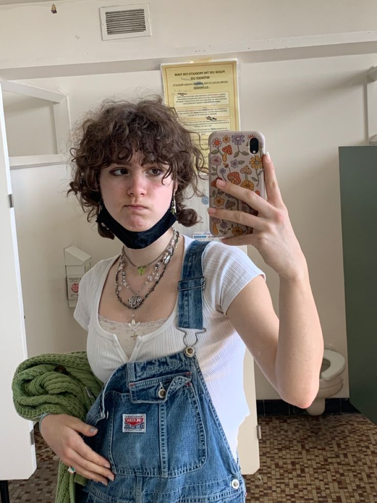 a woman taking a selfie while wearing overalls and holding a cell phone in her hand