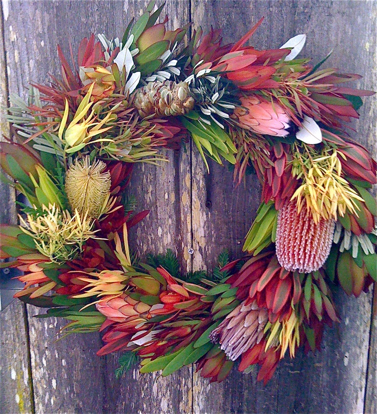 a wreath made out of flowers is hanging on a wooden door frame with an old weathered board behind it