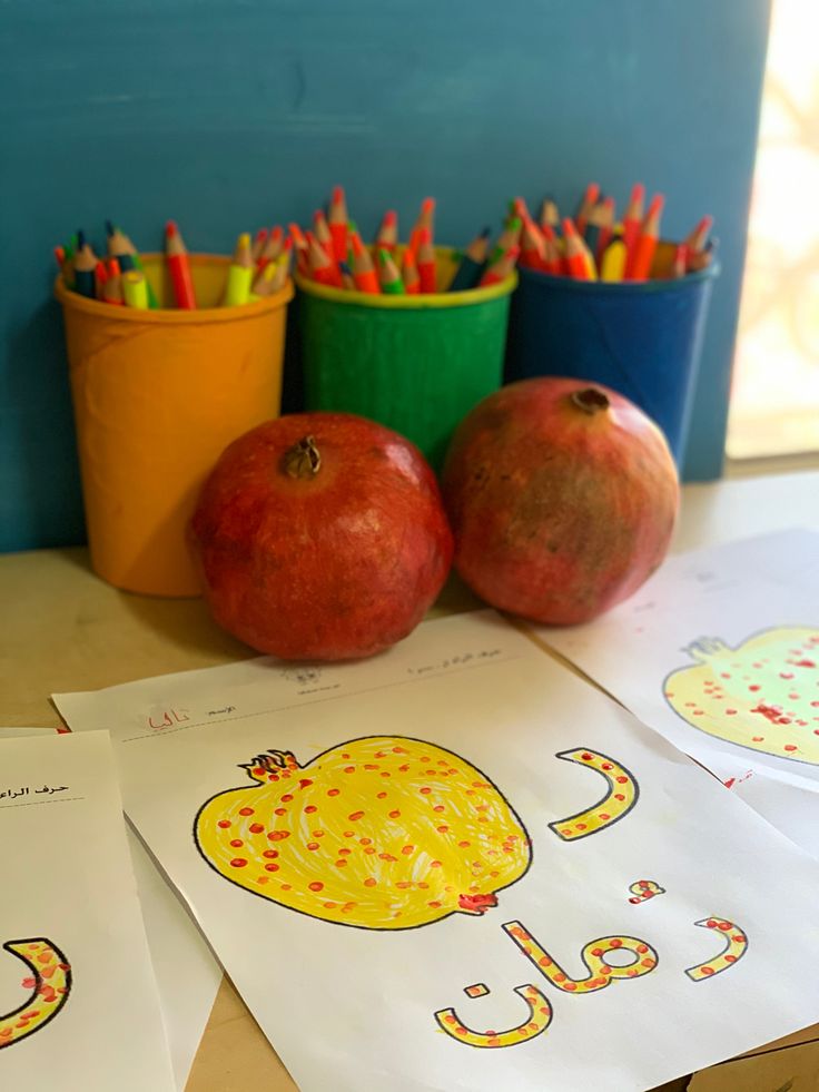 three apples and two oranges sitting on top of a table next to pencils