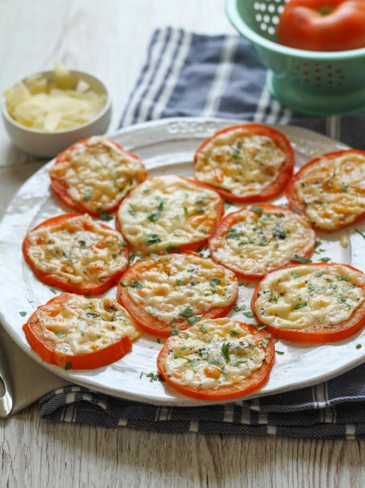 tomatoes with cheese and herbs on a white plate next to a bowl of dips