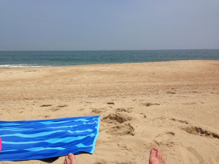 someone is laying on the beach with their feet in the sand and holding a blue towel