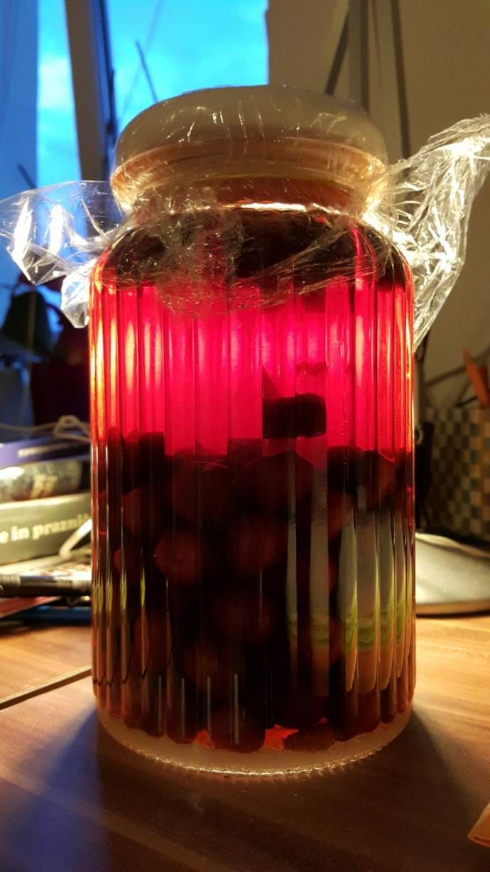 a jar filled with red liquid sitting on top of a wooden table next to a window