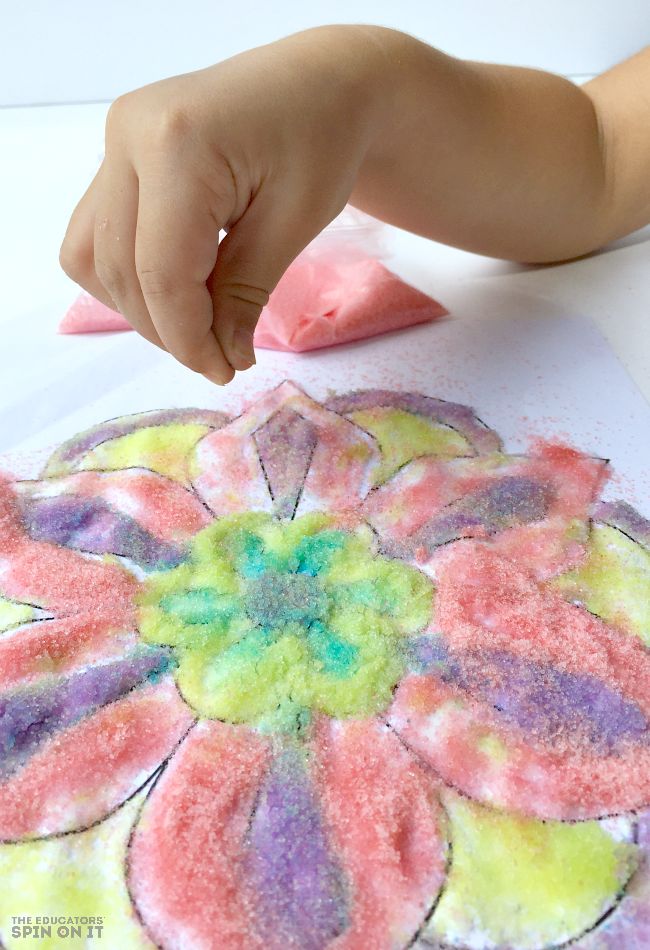 a child's hand is pointing at a flower made out of colored powder