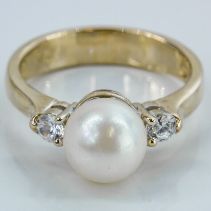 18k Yellow Gold Pearl and CZ Cubic Zirconia Gemstones Ring Embrace the timeless beauty of this 18 Karat Yellow Gold ring adorned with a captivating 7.8mm cultured Pearl and two dazzling Cubic Zirconia stones. The exquisite pearl, measuring 7.8mm in diameter, takes center stage, exuding elegance and sophistication. The shimmering CZ stones gracefully accentuate the ring's shoulders, adding a touch of brilliance. Stamped with "75%" to denote its 18 Karat gold purity, this ring is a testament to it Yellow Gold Cubic Zirconia Pearl Ring For Anniversary, Fine Jewelry Pearl Ring With Cubic Zirconia Center Stone, Fine Jewelry Yellow Gold Cubic Zirconia Pearl Ring, Luxury Yellow Gold Pearl Ring With Center Stone, 14k Gold Round Cut Pearl Ring - Fine Jewelry, Yellow Gold Ring, Center Stage, Gold Pearl, Cz Stone