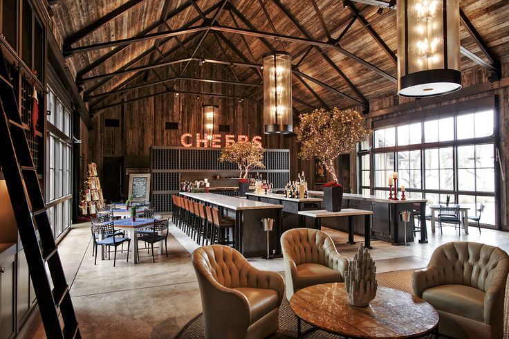 a bar with chairs, tables and stools in a large open room that has wooden walls