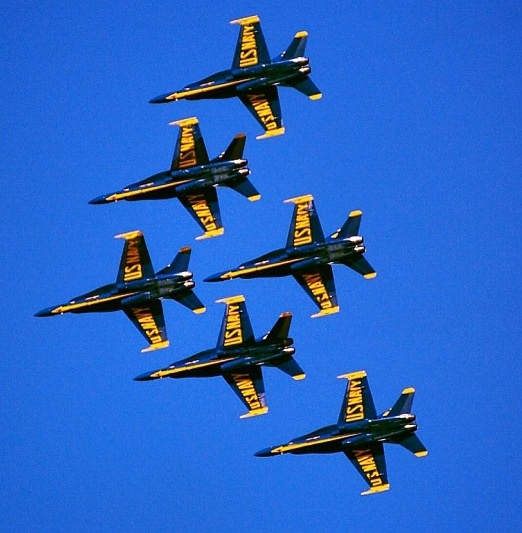 six fighter jets flying in formation against a blue sky with yellow writing on the wings