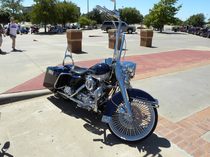 a blue motorcycle parked on the side of a road next to a parking lot filled with people