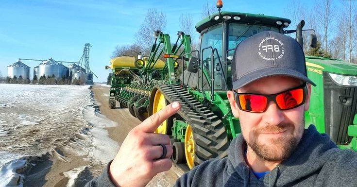 a man wearing sunglasses and a hat standing in front of a tractor on a farm