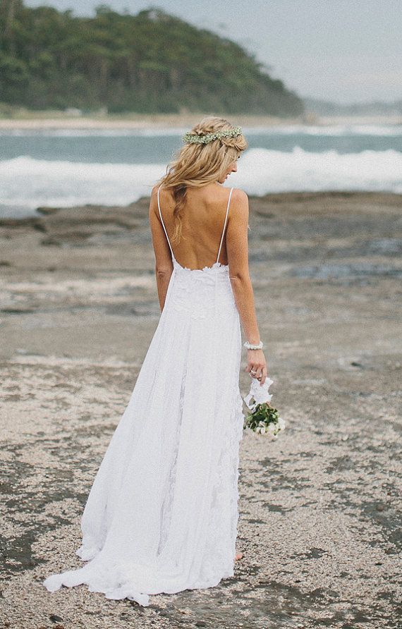 a woman in a white dress standing on the beach with her back to the camera