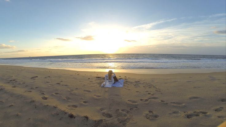 a woman sitting on top of a sandy beach next to the ocean