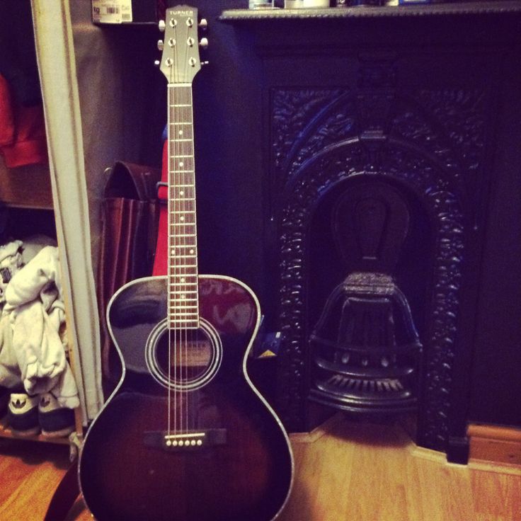 an acoustic guitar sitting on top of a hard wood floor next to a fire place