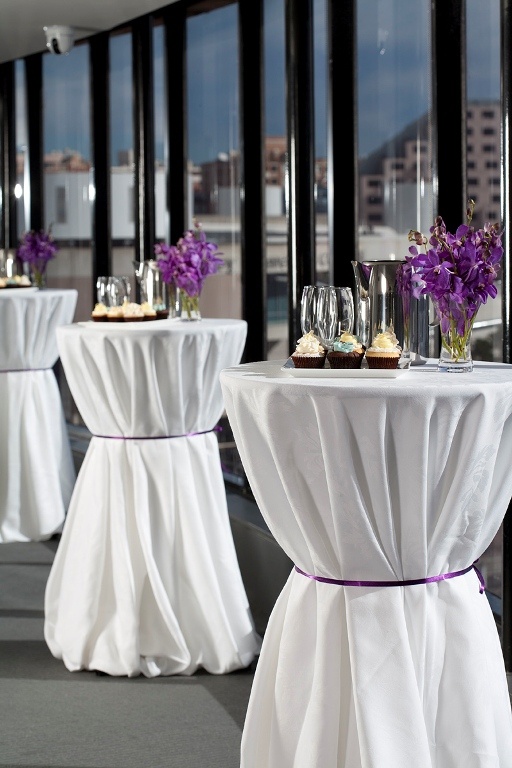 the tables are set up with white linens and purple flowers in vases on them