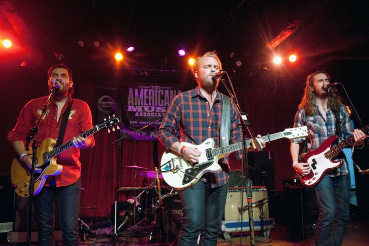 three men on stage playing guitars and singing