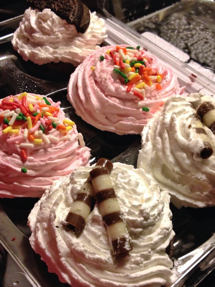 four cupcakes with pink frosting and sprinkles on them in a plastic container