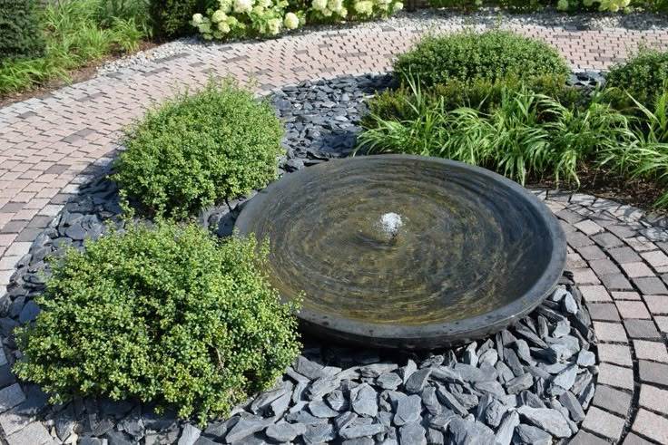 a water fountain in the middle of a brick walkway surrounded by shrubbery and stones