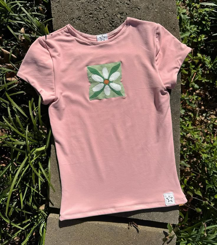 a pink t - shirt with a flower on the front and green leaves in the back