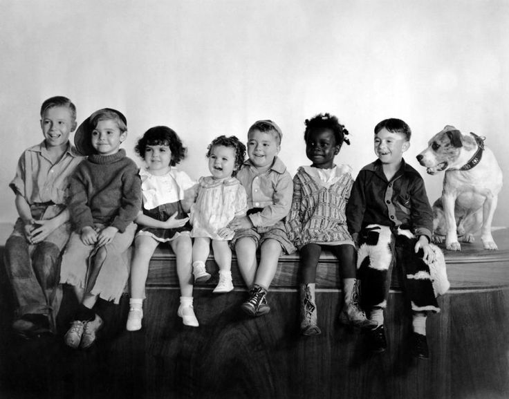 a group of children sitting on top of a wooden bench next to each other in front of a white wall