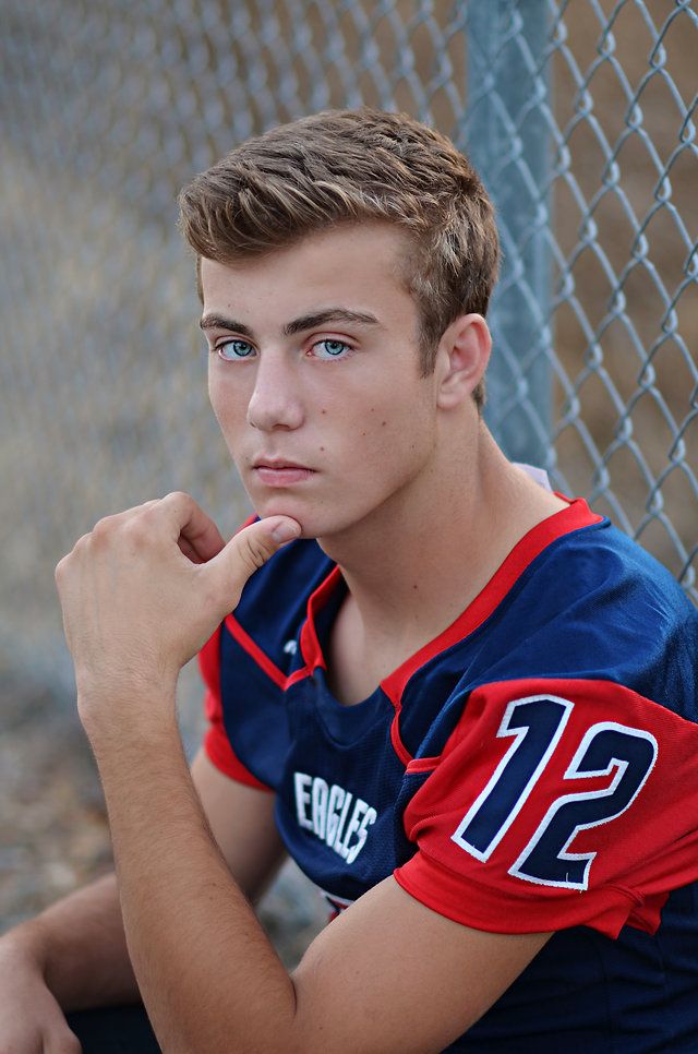 a young man sitting in front of a chain link fence with his hand on his chin