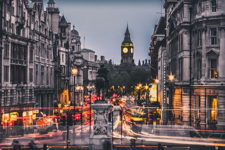 a clock tower towering over a city filled with tall buildings at night, lit up by street lights