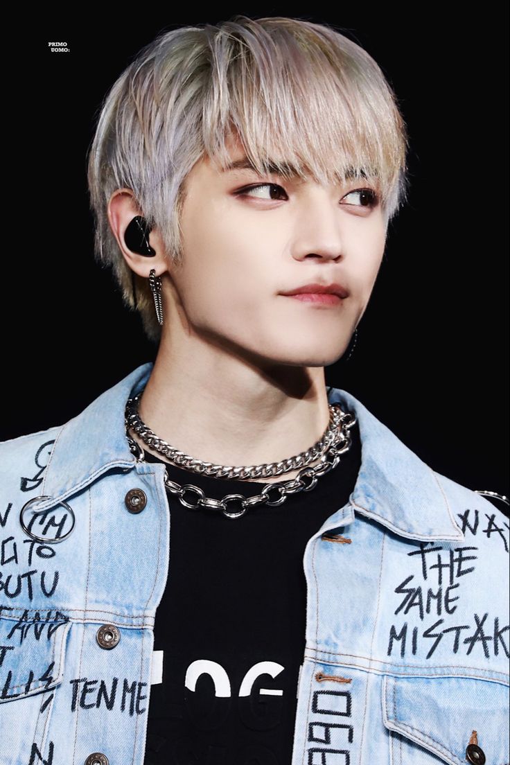 a man with blonde hair and piercings wearing a denim jacket, black t - shirt and chain necklace