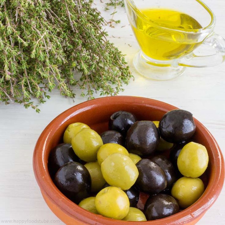 an orange bowl filled with green and black olives next to a bottle of olive oil