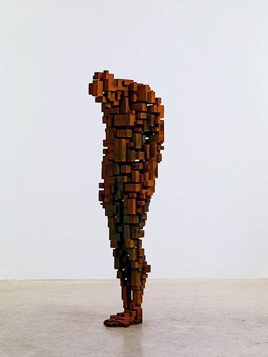 a man made out of wooden blocks standing in front of a white wall with his back turned to the camera