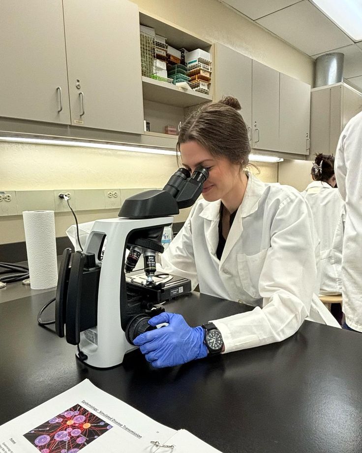 two people in lab coats and gloves looking through microscopes at papers on a table