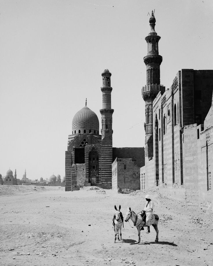 two men on horses in front of an old building with minarets behind them