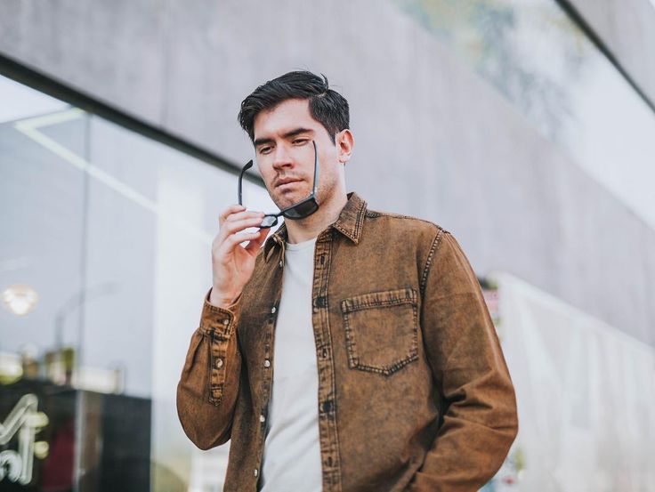 a man wearing a leather jacket and holding a pair of scissors to his face while standing in front of a building