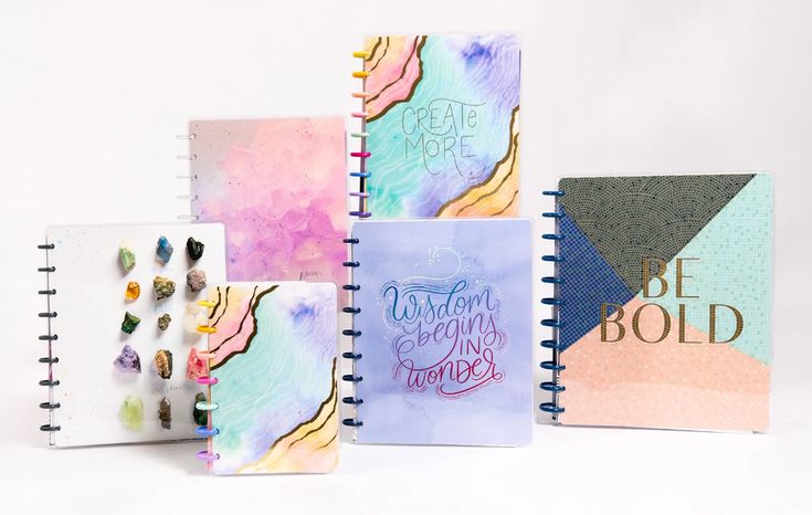 four notebooks with different designs and writing on the pages, all lined up together