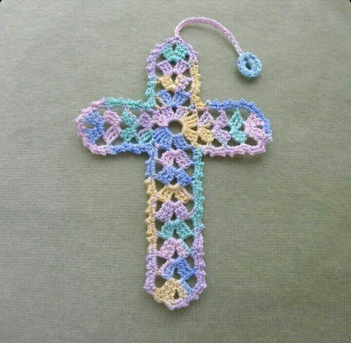 a crocheted cross hanging from a hook on a gray surface with blue trim